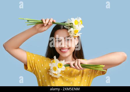 Beautiful young woman with daffodil flowers on blue background Stock Photo