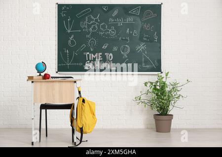 School desk with globe, apple and blackboard on white brick wall in light classroom Stock Photo