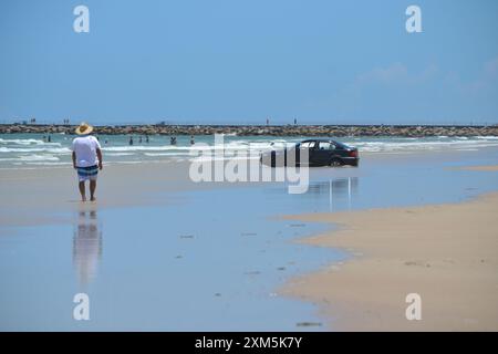 A beachgoer who parked his car at the ocean's edge found himself stuck as the waves rolled in, with onlookers watching the unfolding scene in Florida. Stock Photo