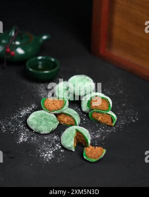 a stack of green mochi with a bite taken out of one on a black plate Stock Photo
