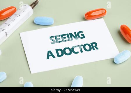 Medicine concept. The inscription SEEING A DOCTOR on a white business card with a syringe and pills lying next to it Stock Photo