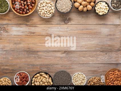 Mixed assorted nuts and seeds in various bowls on wooden table and space for text in the middle. Stock Photo
