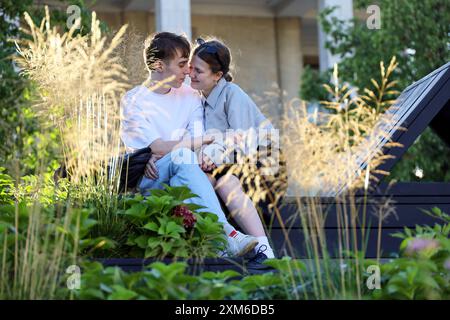 Young couple kissing on a street. Passionate girl and guy embracing sitting in summer park Stock Photo