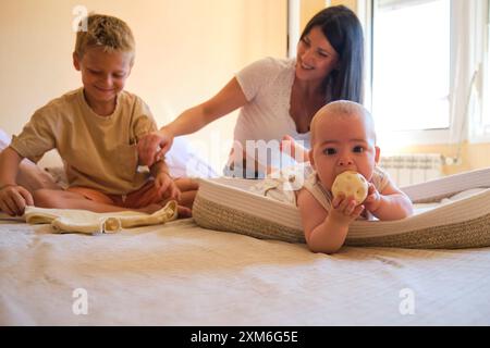 Baby boy playing with toy while mother and brother are sitting on bed Stock Photo