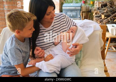 Mother holding newborn baby wrapped in towel with brother Stock Photo
