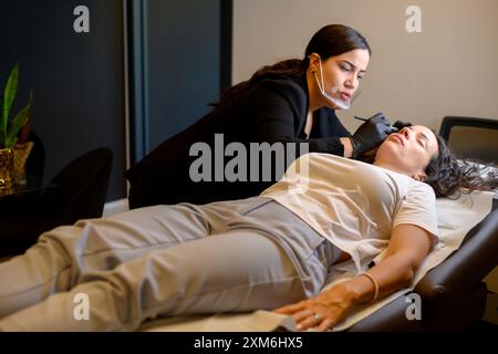 Beautician applying permanent makeup on eyebrows of woman lying down Stock Photo