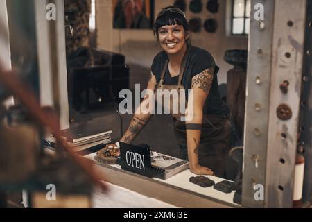 Portrait, woman and entrance of workshop with open sign of metal factory, foundry industry and manufacturing steel. Smile, blacksmith and front desk Stock Photo