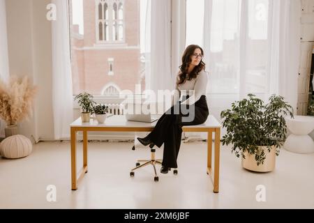 Young Hispanic woman sitting on modern desk with a laptop Stock Photo