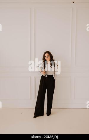 Hispanic woman smiling with notebooks in hand, white paneled wall Stock Photo