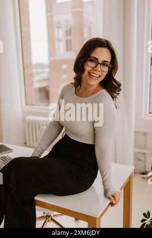 Young Hispanic woman sitting on a modern office desk Stock Photo