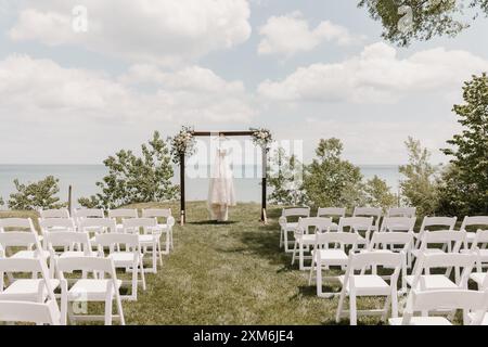 Outdoor lakeside wedding ceremony with a wedding dress hanging on arch Stock Photo