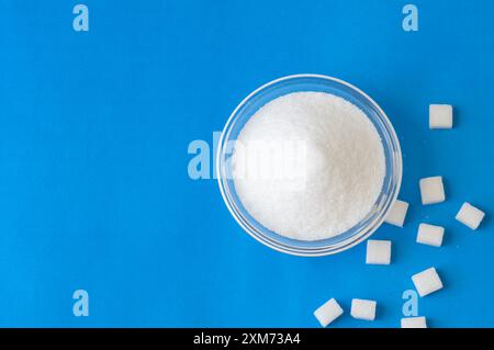 Heap of white granulated sugar with sugar cube on blue background Stock Photo