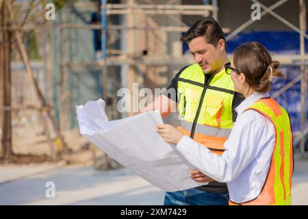 Two construction workers in safety vests reviewing a blueprint at an outdoor building site, collaborating and planning work. Stock Photo