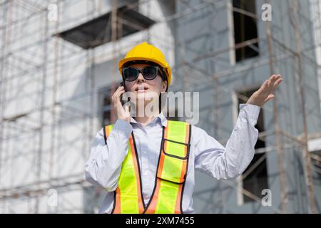 A construction worker wearing a safety helmet and vest speaks on the phone, emphasizing communication and safety at a worksite. Stock Photo