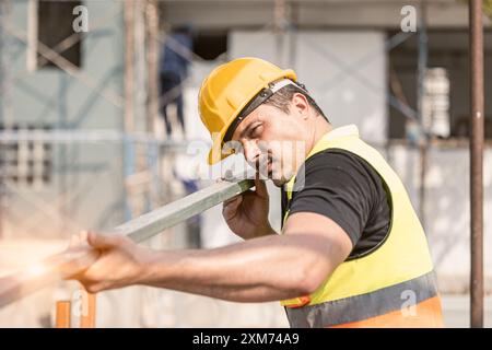 A dedicated construction worker in a yellow hard hat and safety vest focuses on his task at a construction site. Stock Photo