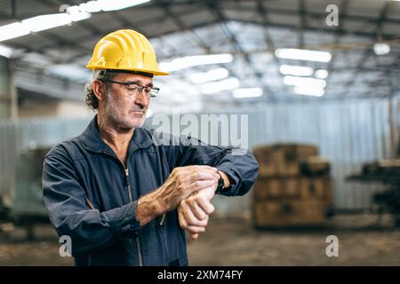 Engineer worker worry looking at wristwatch working time clock. Industry factory late working hours concept. Stock Photo