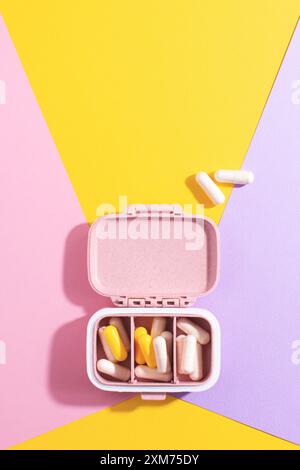 Creative medical and health care composition: open pill box with white and yellow capsules on colourful background. Stock Photo