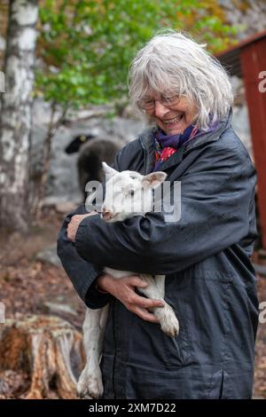 A middle-aged woman has a newborn lamb in her arms and smiles broadly, photo: Bo Arrhed Stock Photo