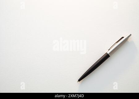 Black And Silver Classic Ballpoint Pen Laying On White Paper Texture. Copy Space Background Stock Photo