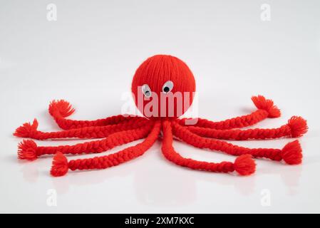 Red octopus puppet toy on a white background, handmade in soft wool. This cute stiffed doll is knitted with love for fun. Stock Photo