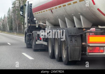 A truck with a semi-trailer tanker transports a dangerous chemical cargo of acid and alkali along a country road in the spring. Stock Photo