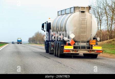 A tanker semi-trailer truck transports a dangerous cargo of gasoline, diesel fuel and petroleum products on the road against the backdrop of the sun. Stock Photo