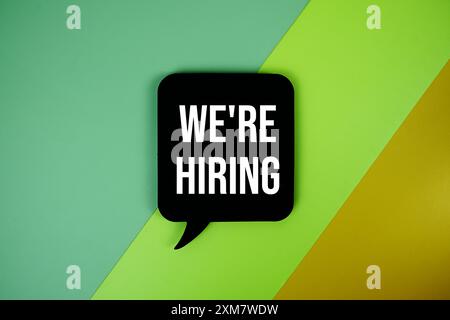 We Are Hiring text on speech bubble top view on green and yellow geometric background Stock Photo