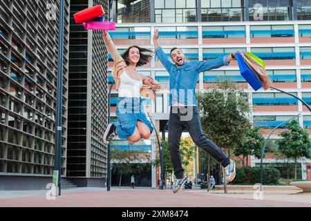 Young couple jumping, raising their arms while holding shopping bags at the mall. Happy customer people skipping on a store. Enthusiastic boyfriend and excited girlfriend leaping. Friends buying. High quality photo Stock Photo