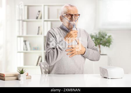 Elderly man with breathing problem sitting at a table and using a nebulizer at home Stock Photo