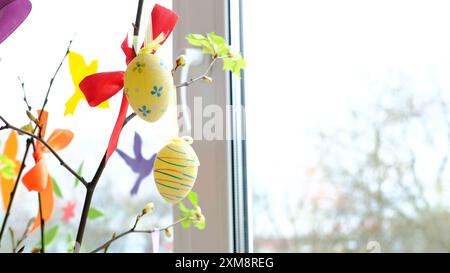 Brightly decorated Easter eggs and ribbons on willow branches by a window. Stock Photo