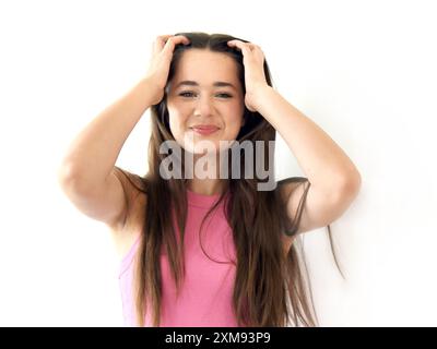 Female teen grabs her head in frustration.  She has long dark hair and is wearing a pink top. She is inside in white room. Stock Photo