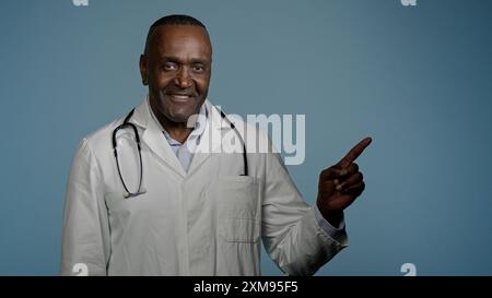 African American man doctor medical worker in white coat male healthcare employee medic customer in studio blue background pointing index finger Stock Photo