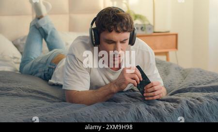 Caucasian European young man guy male cheerful listen music on headphones audio playlist sing holding mobile phone smartphone gadget device technology Stock Photo