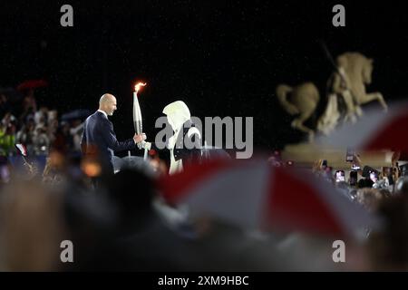 (240726) -- PARIS, July 26, 2024 (Xinhua) -- The mysterious torchbearer hands over to Former French Footballer Zinedine Zidane at the Place du Trocadero during the opening ceremony of the Olympic Games Paris 2024 on July 26, 2024 in Paris, France. (Cameron Spencer/Getty Images/Pool via Xinhua) Stock Photo