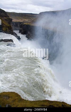 Water cascading into the canyon at Gullfoss waterfall in Iceland, making walls of spray. The Hvita river in Iceland flows southward before cascading 32 metres (105 feet) down Gullfoss' two stages. During the summer, approximately 140 cubic metres (459 cubic feet) of water surge down the waterfall every second. Stock Photo
