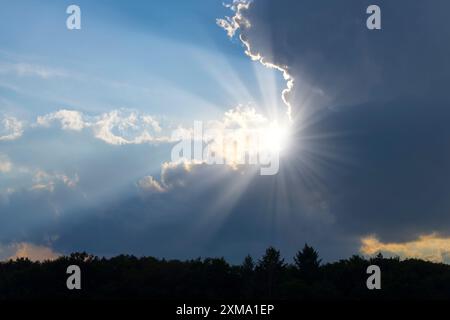 Rain clouds with sun shining through, sunbeams, blue sky, forest Stock Photo