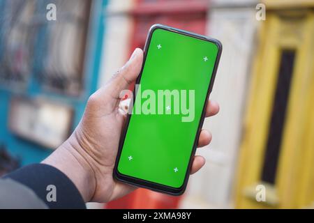 A man in an urban setting holds a smartphone with a green screen, showcasing modern technology Stock Photo