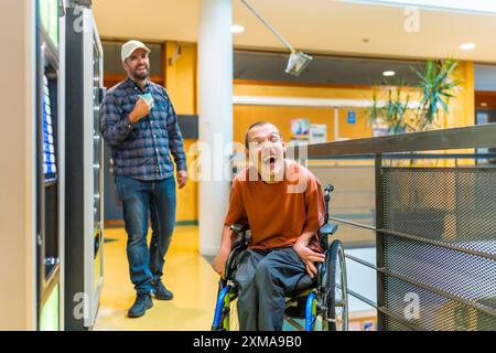 Man with cerebral palsy laughing next to coworker during a work break walking into vending machines Stock Photo