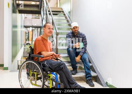 Man with cerebral palsy talking with a work colleague indoors in a modern coworking with staircase Stock Photo