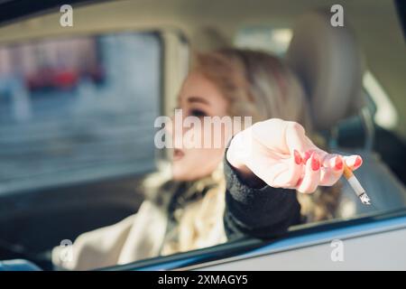 Young woman is throwing a cigarette butt out of the car window,  contributing to pollution and showcasing the issue of cigarette butt litter  Stock Photo
