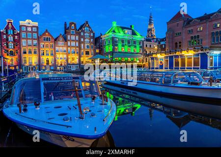 Canal houses on the Damrak, in the centre of the old town of Amsterdam, harbour, starting point of many canal tours, in the evening, church tower of Stock Photo
