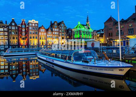 Canal houses on the Damrak, in the centre of the old town of Amsterdam, harbour, starting point of many canal tours, in the evening, church tower of Stock Photo