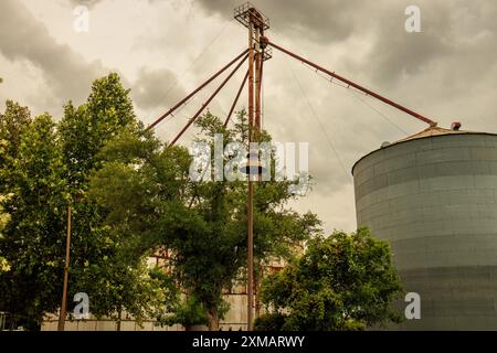 Grain mill in Buda, Texas, featuring a large corrugated silo and rusty framework against a cloudy sky, rustic charm, agricultural-industrial history. Stock Photo