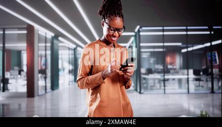 African-American Woman Professional Using Smartphone In Office As A Customer Service Representative Browsing New App For Sales Management. Stock Photo