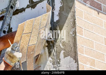 Installing brick veneer outside, construction worker decorates facade of house with exterior panel of fake thin brick. Stock Photo