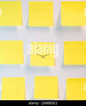A yellow piece of paper with a smiley face drawn on it. The paper is placed next to other yellow pieces of paper Stock Photo