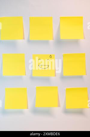 A yellow post it with a smiley face on it. There are nine other yellow post it's on a white background Stock Photo