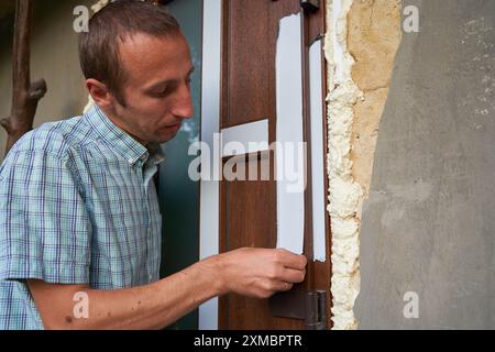 a man removes masking tape from a new door that has just been installed Stock Photo
