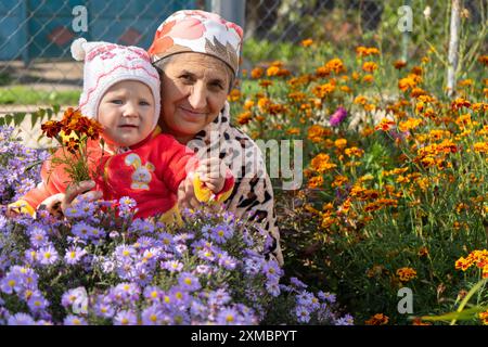 happy senior woman sitting with baby in alpine alpine flowers Stock Photo