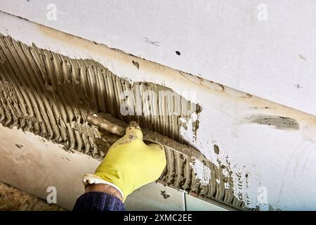 Builder tiler applies adhesive cement mortar to wall using comb trowel. Stock Photo